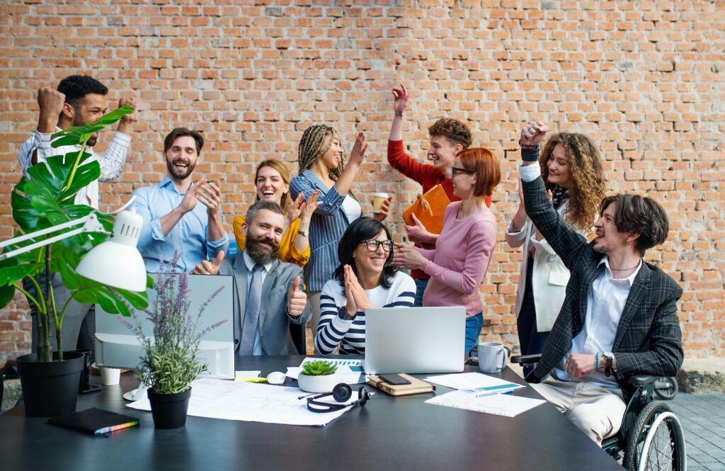 Eine Gruppe von Geschäftsleuten feiert in einem modernen Büro einen Erfolg, lächelt, applaudiert und zeigt Freude bei ihrer Arbeit.
